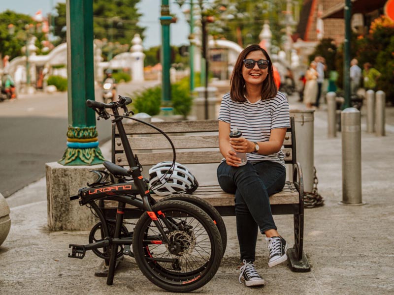 A woman happily sits with her folded state foldable bike after enjoying a short ride in the city A woman happily sits with her folded state foldable bike after enjoying a short ride in the city