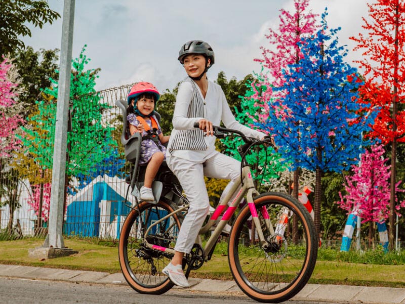 A mom and her daughter cycling through the street surrounded by colorful trees A mom and her daughter cycling through the street surrounded by colorful trees