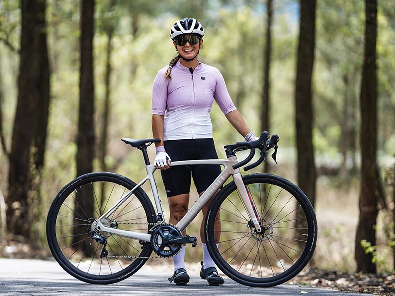 A woman stands with her road bike after completing a ride in the hills A woman stands with her road bike after completing a ride in the hills